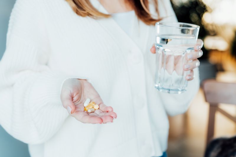 Frau hält Nahrungsergänzungsmittel in der Hand und ein Glas Wasser, symbolisch für die Einnahme von Supplements zur Unterstützung der Gesundheit.